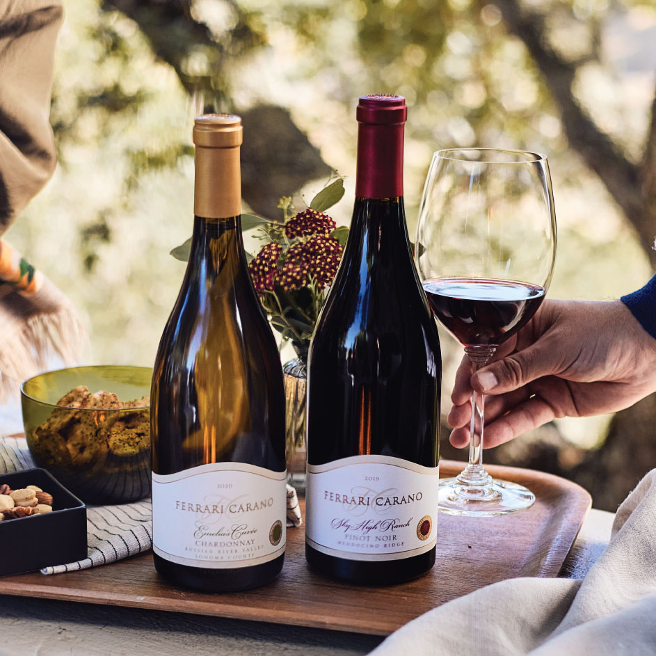 Two bottles of Ferrari Carano Wines on a table with a persons hand shown holding a glass of red wine